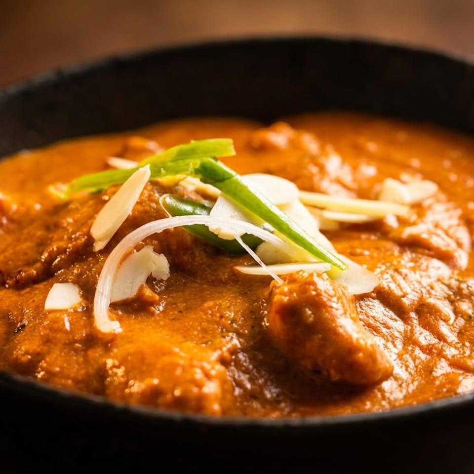 Close-up of a black bowl filled with rich orange curry, garnished with sliced onions and green herbs.